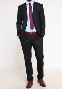 Svart kostym med smal passform, ljusblå skjorta, röd prickig slips, brun läderbälte och bruna skor. Slät tygtextur.