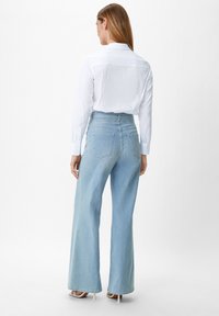Jeans a vita alta blu chiaro, larghi e con una finitura testurizzata, caratterizzati da tasche posteriori e dettagli di cucitura sottili. Abbinati a una camicia bianca.