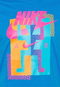 Nike Air 94-logotyp med rosa Nike-text och swoosh över orange och blå abstrakta former på blå tygbakgrund.