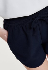 Námořnické modré šortky vyrobené z měkké, lehké látky. Obsahují elastický pas s tkaničkou a postranní kapsy. Hladká textura.