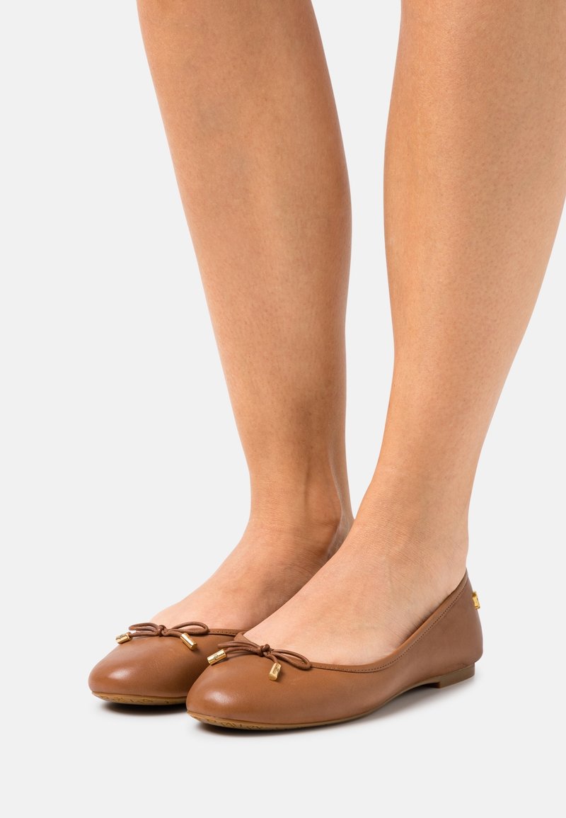 Hnědé kožené baletní byty s kulatou špičkou, detailem mašle a malými zlatými akcenty na podpatku. Plochá podrážka a hladký povrch.