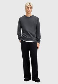 Sudadera de algodón gris oscuro con cuello redondo, puños de canalé y un pequeño logo en el pecho, combinada con pantalones negros de corte holgado.