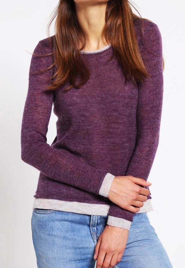 Fioletowy sweter dziany z okrągłym dekoltem, długimi rękawami i beżowymi lamówkami na mankietach oraz na dole. Wykonany z miękkiej, teksturowanej tkaniny. Noszony z niebieskimi dżinsami.