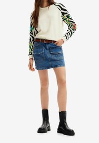 Pletený svetr s bílou bodou a černými rukávy se zebřím vzorem; džínsová sukně modré barvy, přední kapsy a dekorativní švy; černé kotníkové boty.