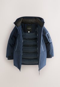 Marineblå dunjakke med lynlåslukning foran, stor hætte og flere lommer. Har quiltet foring og diskret branding indvendigt.