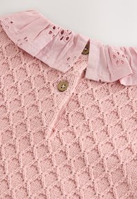 Pink strikbluse med et tekstureret diamantmønster, en flæsekrave med blomsterudskæringer og to runde brune knapper.
