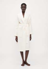 Hvit, fysj bathrobe med sjalkrage, belte i midjen og to frontlommer. Midtlengde design med en myk, teksturert overflate.