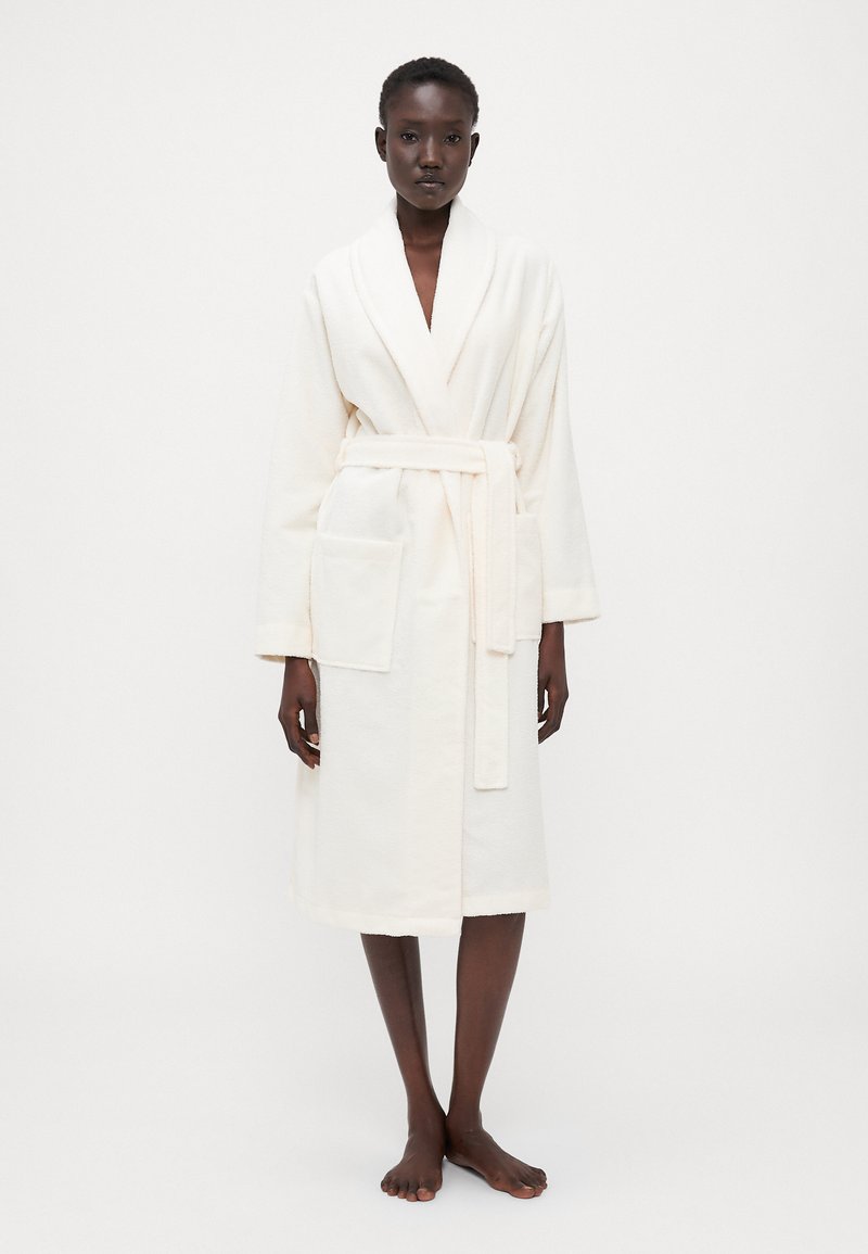 Hvit, fysj bathrobe med sjalkrage, belte i midjen og to frontlommer. Midtlengde design med en myk, teksturert overflate.