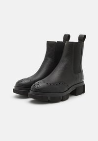 Stivali Chelsea in pelle nera con superficie testurizzata, dettagli perforati sulla punta e suola in gomma spessa per un'altezza aggiuntiva.