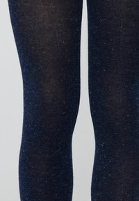 Collant blu navy con una texture liscia, caratterizzati da piccole macchie discrete. Il tessuto appare leggermente trasparente, offrendo un look aderente.