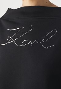 Černá mikina s kurzívním designem ozdobeným stříbrnými rhinestones, který zvýrazňuje klasické logo na zádech.
