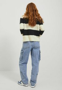 Maglione a righe in crema e nero, abbinato a jeans cargo blu con tasche laterali e sneaker bianche con dettagli navy.