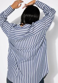 Camicia a righe blu e bianche con una vestibilità ampia, caratterizzata da maniche lunghe e un orlo curvo. Tessuto testurizzato con righe orizzontali in contrasto.