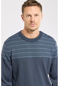 Pull bleu marine avec un motif en maille texturé, featuring des rayures horizontales bleu clair et quatre boutons sur l'épaule gauche.