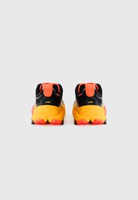 Baskets de sport noires et jaunes avec des accents orange, dotées d'une tige texturée, d'une semelle rembourrée et d'un motif de semelle distinctif.