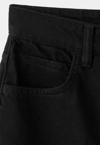 Jean en denim noir en gros plan montrant la ceinture, les passants de ceinture et la poche avant avec des détails de couture visibles.