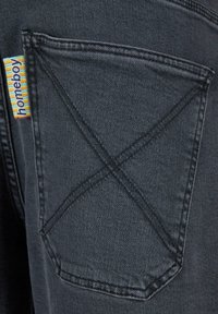 Schwarzer Denim-Stoff mit einer Hintertasche, die ein X-Stich-Muster aufweist, sowie einem mehrfarbigen "Homeboy"-Label an der Kante.