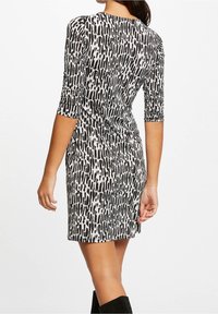 Schwarzes und weißes, figurbetontes Kleid mit einem strukturierten, abstrakten Muster, knielangen Ärmeln, Rundhalsausschnitt und einem leicht ausgestellten Saum.