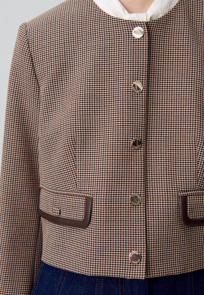 Veste courte à motif pied-de-poule marron avec boutons en métal argenté et accents en simili cuir marron sur les poches et l'ourlet. Détail de collier blanc inclus.