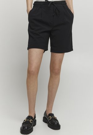 Zwarte shorts gemaakt van een zacht stof met een elastische tailleband en een trekkoord. Ze hebben zijzakken en een relaxte pasvorm, eindigend boven de knie.