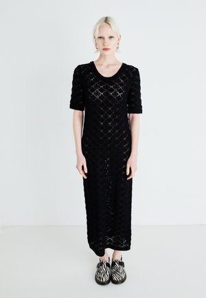 Abito nero a maglia con un motivo a rombi, maniche corte e scollo rotondo. Abbinato a scarpe a righe zebrate in bianco e nero.
