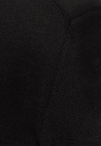 Nahaufnahme von schwarzem Strickstoff, der die detaillierte Textur zeigt, mit einer sichtbar diagonalen Naht.