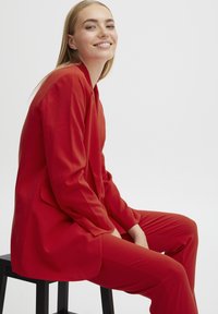 Completo rosso su misura con una vestibilità comoda, caratterizzato da maniche lunghe, revers a punta e tasche laterali. Texture liscia e colore audace.
