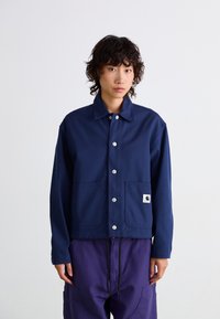 Veste bleu marine en tissu robuste, dotée d'un col, de boutons-pression et de deux poches avant avec un petit logo.