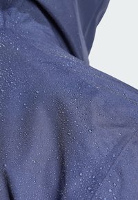 Tissu imperméable marine avec une surface texturée, présentant de nombreuses petites gouttes d'eau, indiquant une résistance à l'eau et une utilisation en extérieur.