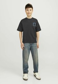 Camiseta de algodón negra con gráfico azul en el pecho, combinada con jeans de mezclilla azul claro y zapatillas blancas con rayas negras.