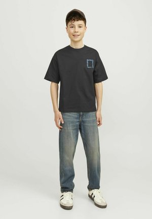 Camiseta de algodón negra con gráfico azul en el pecho, combinada con jeans de mezclilla azul claro y zapatillas blancas con rayas negras.