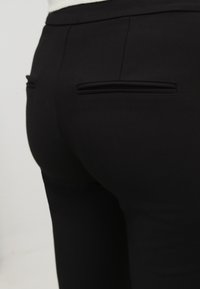 Černé kalhoty na míru s hladkým, matným povrchem, které mají dvě kapsy na švech vzadu a štíhlý design pro dobře padnoucí vzhled.