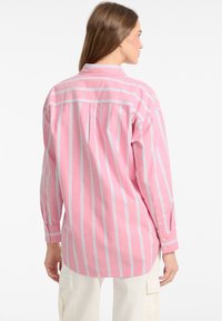 Camicia button-up rosa con strisce verticali bianche e blu, caratterizzata da colletto, maniche lunghe e vestibilità comoda. Dettagli di cucitura semplici.