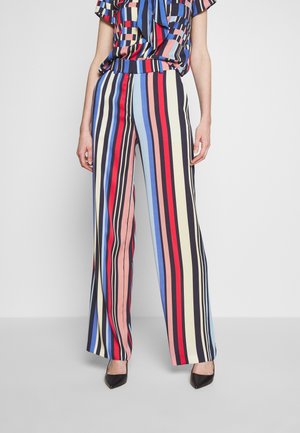 Pantalons à larges jambes avec des rayures verticales en rouge, bleu, rose et noir. Tissu léger, taille haute et coupe décontractée, associés à des talons noirs.