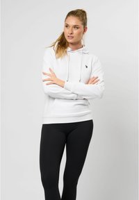 Hvit hettegenser med snøring, med en liten svart logo på brystet. Kombinert med svarte leggings, mot en nøytral bakgrunn.