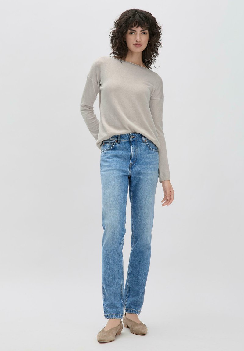 Lichtgrijze lange mouwen top, blauwe rechte jeans en beige schoenen. De top heeft een brede halslijn, terwijl de jeans een klassiek 5-pocket ontwerp hebben.