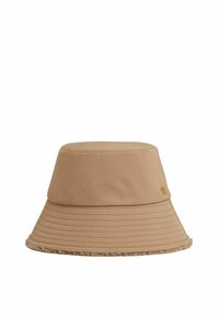 Beige bucket hat made of soft fabric, featuring a wide brim with a textured trim, ribbed detailing, and a small gold logo accent.