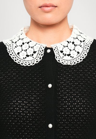 Black cardigan with a knitted texture, featuring a white lace collar adorned with floral patterns and three pearl buttons at the front.
