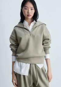 Oversized, licht olijfgroene sweatshirt met een halve ritssluiting bij de kraag, geribde manchetten en een textuurstof, gelaagd over een witte blouse.