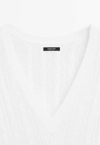White knitted sweater with a V-neck. The fabric features a cable knit pattern, and the label reads 'Massimo Dutti, Made in Turkey.'
