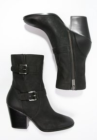 Botas de cuero negras hasta el tobillo con un tacón de bloque curvado, cremallera lateral y hebillas decorativas en el eje. Textura suave y diseño elegante.