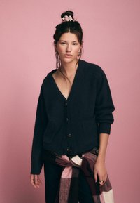 Dunkelblauer gestrickter Cardigan mit großen Knöpfen, V-Ausschnitt und Taschen. Kombiniert mit einem karierten Schal in Burgunder, Creme und Rosa.