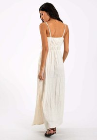Robe maxi en tissu blanc texturé avec des bretelles fines ajustables, corsage ajusté et détails de fente sur le côté. Conception légère et jusqu'au sol.