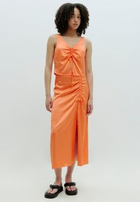 Tweedelig outfit in feloranje satijn. Bevat een gecropte top met plooien en een bijpassende midi-rok met een zijsplit en geplooide details.