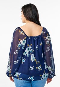 Blusa floreale blu navy con tessuto trasparente. Presenta maniche lunghe a sbuffo, scollatura quadrata e motivi floreali in azzurro chiaro e bianco.