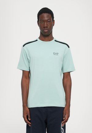 Tricou verde menta deschis cu un guler rotund, accente negre pe umeri și logo-ul EA7 pe piept. Mâneci scurte, textură netedă.