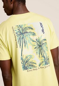 Geel katoenen t-shirt met een grafische print van palmbomen op de achterkant, met de tekst "Italiaanse Rivièra Ligurië" en "Elk Stap, Een Nieuwe Reis."