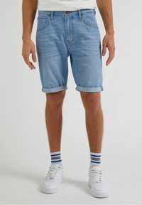 Ljusblå denimshorts med upprullade fållar, med en klassisk femfickdesign. Bärs med vita sneakers och randiga strumpor.