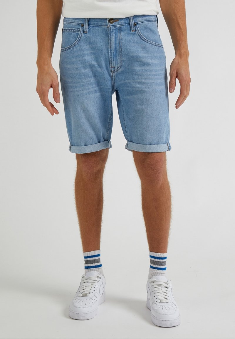 Ljusblå denimshorts med upprullade fållar, med en klassisk femfickdesign. Bärs med vita sneakers och randiga strumpor.
