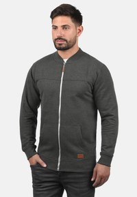Grå zip-up sweatshirt med ribbede manchetter og nederste kant, med en glat tekstur, to frontlommer og et lille logomærke på den nederste front.